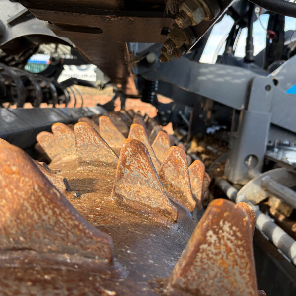 Close-up of rusted, jagged steel teeth from industrial machinery, with a gray metal frame in the background.