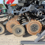 Close-up of a farm seeder’s rusted disk blades and metal framework with hoses and bolts visible