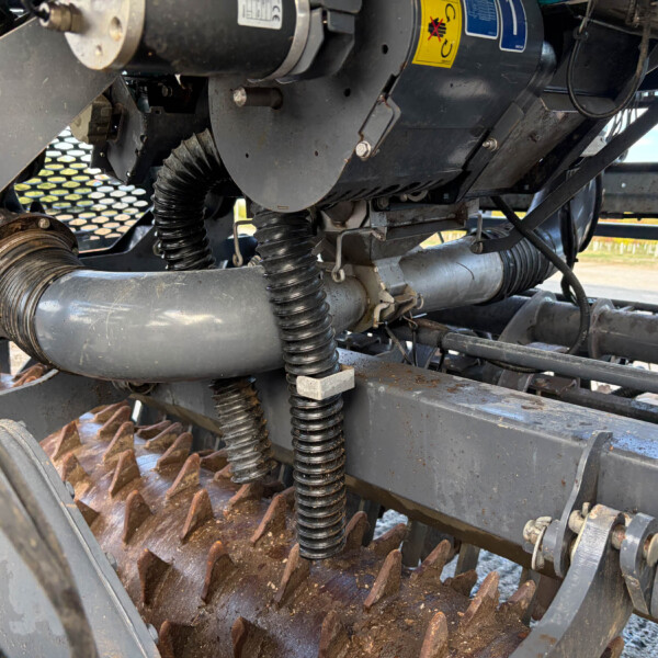 Close-up of heavy machinery internals: rusted cog belt, hoses, and metal framework visible under equipment set-up.