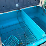 Open blue dumpster interior with metal grate floor and teal panels, straps hanging along the sides, outdoor setting.