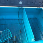 Open blue dumpster interior with wire-mesh floor panels and vertical partitions, straps along the sides, and a lid visible at the top edge of the image.