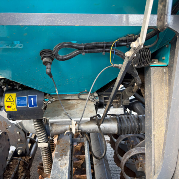 Blue industrial machine body with black corrugated hoses, cables, and metal framework visible in a service area.