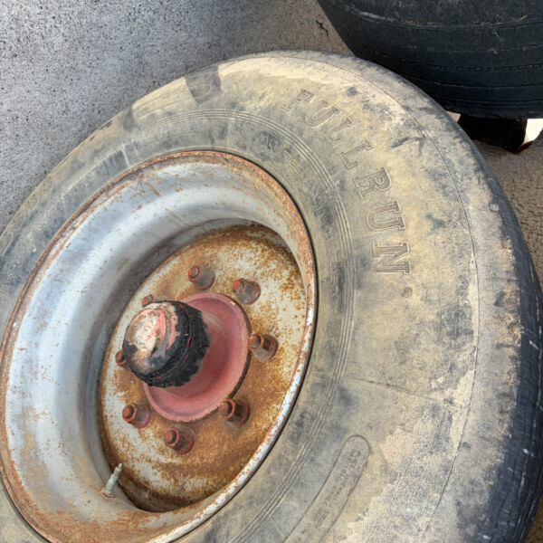 Close-up of a large, dusty tire with a rusted red metal hub, resting on a dusty ground surface.
