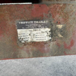 Close-up of a rusted red trailer body with a weathered data plate showing model and weight information.