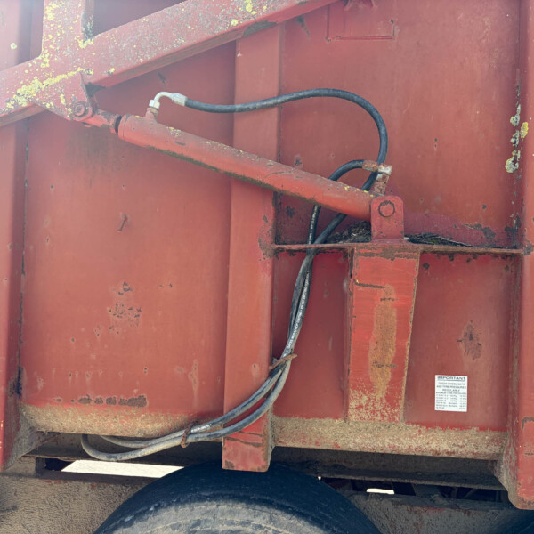 Close-up of a red metal trailer side with black hydraulic hoses secured to brackets, showing dirt and rust.