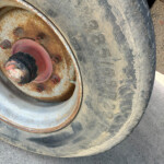 Close-up of a dusty, weathered tractor tire and rusted wheel hub with red bolts protruding from the rim.