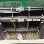 Close-up of hydraulic hoses and fittings mounted to a heavy equipment trailer, with safetyLabels and a green sign above.