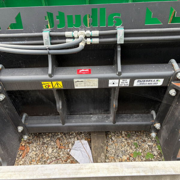 Close-up of hydraulic hoses and fittings mounted to a heavy equipment trailer, with safetyLabels and a green sign above.