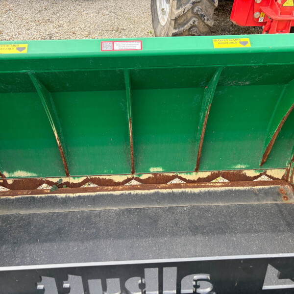 Green dump trailer bed with rusted support ribs, viewed from above, on a gravel surface and asphalt edge nearby.