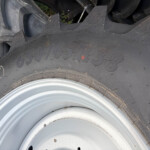 Close-up of a large off-road tire with thick, rugged tread and a rusted metal wheel rim nearby.