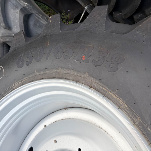 Close-up of a large off-road tire with thick, rugged tread and a rusted metal wheel rim nearby.