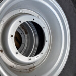 Close-up of a silver steel wheel/rim with several bolt holes, mounted with a black tire; small rust spots present on the rim edge.