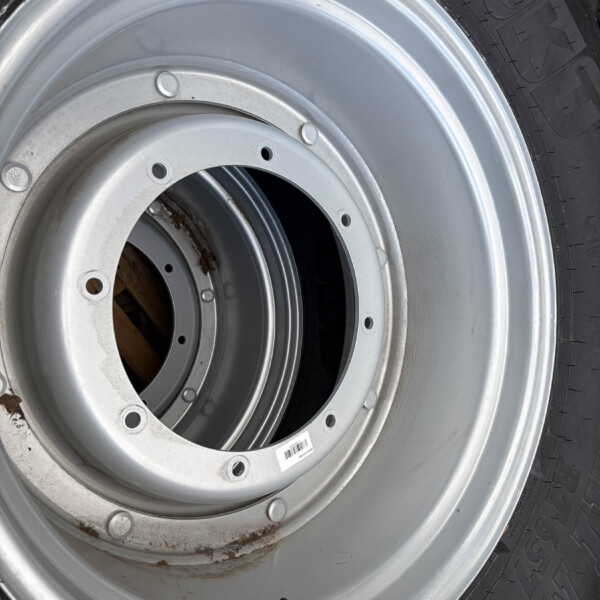 Close-up of a silver steel wheel/rim with several bolt holes, mounted with a black tire; small rust spots present on the rim edge.