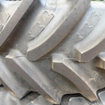 Close-up of stacked large rubber tires with deep diagonal treads, showing worn surfaces and metal rivets edgewise.