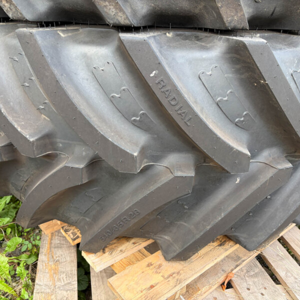 Stack of large black rubber tracks with raised treads resting on wooden pallets outdoors, some dirt visible on the surfaces.