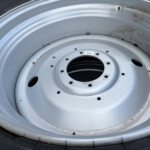 Close-up of a light gray steel wheel rim with multiple lug holes, inside a black tire; small rocks and dirt cling to the rim edge and inner surface.
