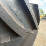 Close-up of stacked black steel plates with rivets, showing curved edges and worn metal texture in an outdoor yard.