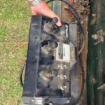 Farmer's hand on a dusty tractor-style control panel with multiple levers outdoors. (informative)