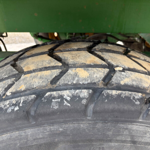 Close-up of a dusty heavy-duty tire with deep treads beneath a green agricultural machine.