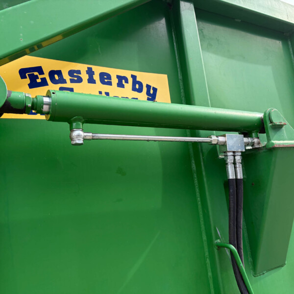 Close-up of a green industrial machine with a yellow warning label and hydraulic arm components.