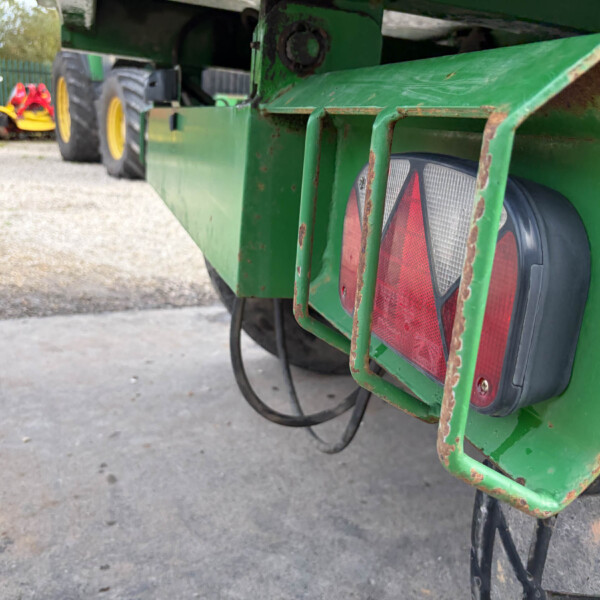 Close-up of a green trailer rear with red reflective lights and rusted metal frame near a tire edge