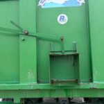 Close-up of a green industrial container door with a rusted support arm and a circular Russell's sticker nearby.