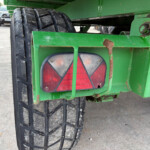 Close-up of a green trailer showing a large rugged tire and a rusted metal frame with a red tail light visible behind the frame.