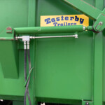 Close-up of a green trailer chassis with a hydraulic cylinder, hoses, and a yellow 'Easterby Trailers' label.