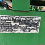 Worn metal nameplate on green machinery with serial and weight information visible (rusty screws)