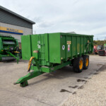 Green agricultural machinery and a large green trailer parked in a lot beside a building with a yellow-blue Russell's sign above the doorway.