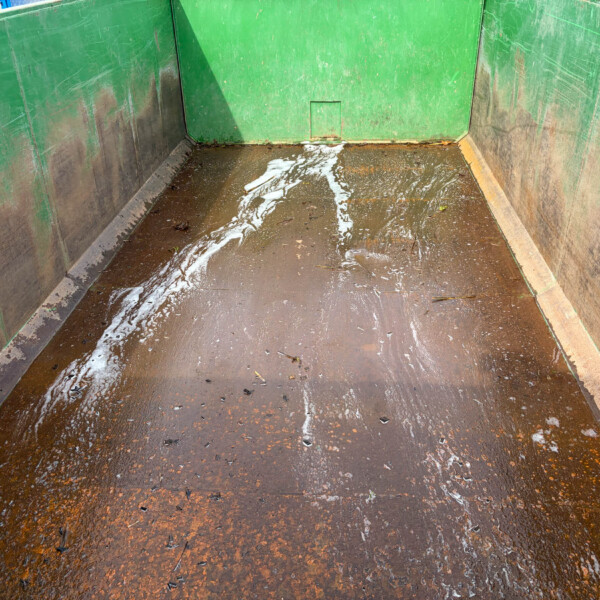 Green metal dumpster interior filled with muddy water and scattered debris at the bottom.