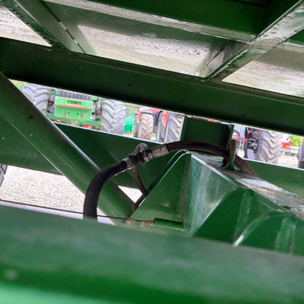 Close-up of green metal farm equipment frame with hydraulic hose and a tire visible in the background