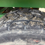 Close-up of a muddy tire tread with a green agricultural machine frame in the background.