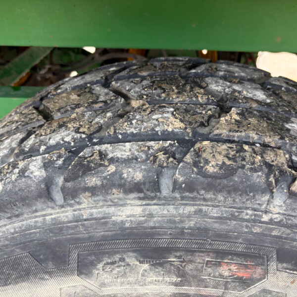 Close-up of a muddy tire tread with a green agricultural machine frame in the background.