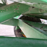 Close-up of green metal beams with rust specks, a wheel visible through the structure in the background.