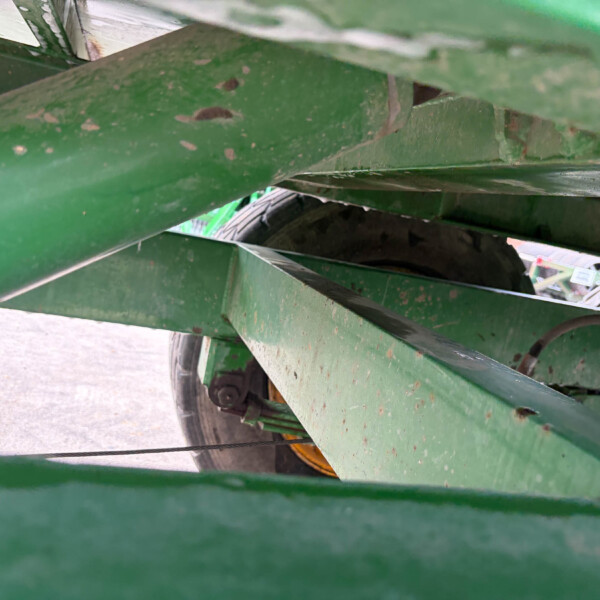 Close-up of green metal beams with rust specks, a wheel visible through the structure in the background.