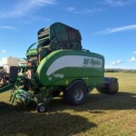 Green McHale Fusion VARIO round baler in a grassy field under a clear blue sky, parked with its front intake and hoses visible