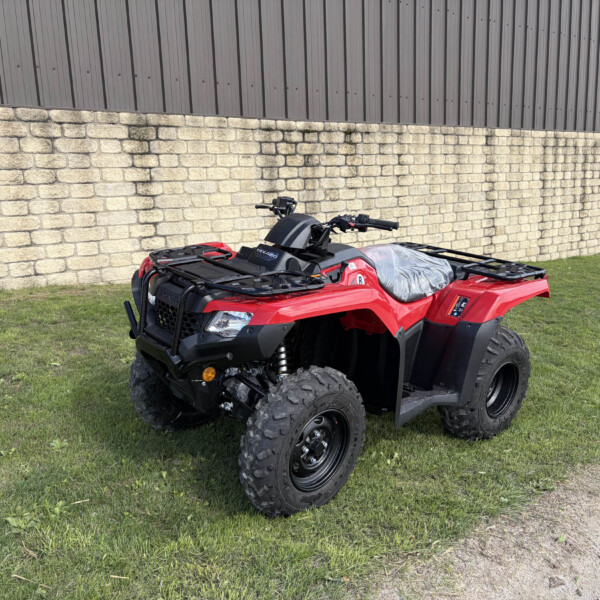 Red ATV parked on grass beside a beige stone wall and gray corrugated metal building.
