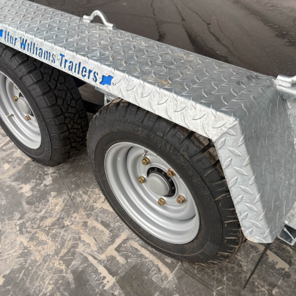 Diamond-plate trailer bed with dual-axle wheels and tires visible, showing a sturdy metal frame and wheel hubs. Note: blue lettering on the side indicates the trailer brand.