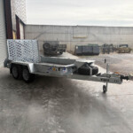 Industrial loading area with a flatbed trailer beside a corrugated metal wall and concrete building in the background