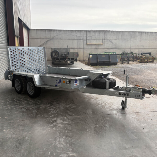 Industrial loading area with a flatbed trailer beside a corrugated metal wall and concrete building in the background