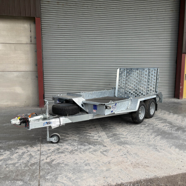 Industrial trailer with a metal ramp and spare tire parked in front of a large corrugated metal shutter doors.