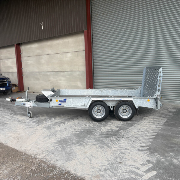 Blue Isuzu pickup parked beside a large metal warehouse with corrugated doors and a silver trailer in a construction yard.