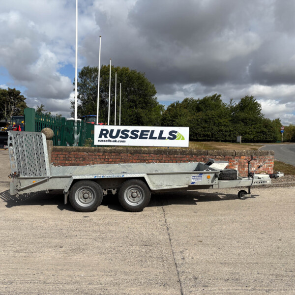 trailer loaded with metal panels sits on a paved lot beside a green fence and a Russell's sign with the website russells.uk.com, under a cloudy sky.