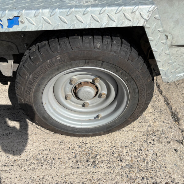 Close-up of a vehicle wheel and tire beneath a diamond-plate metal fender on a trailer or utility vehicle. It shows a steel rim with lug nuts and a rugged tread tire.