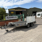 Agricultural workshop with a Russell's sign on a green building and a parked tractor to the right under a blue sky