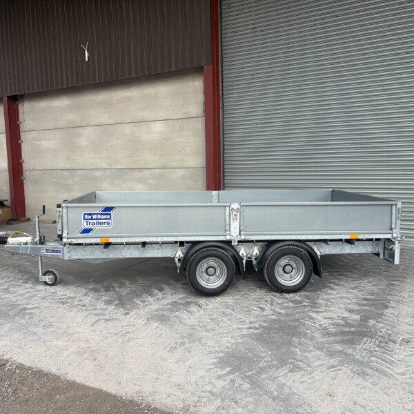 A metal flatbed trailer parked indoors next to a blue Isuzu vehicle, with a large roller shutter door in the background.