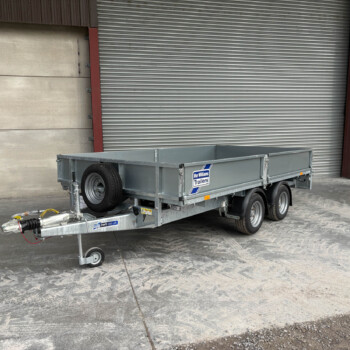 Metal utility trailer with twin axles and a spare wheel, parked before a large gray corrugated roller door; yellow door on the right side.