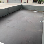 Empty metal flatbed trailer interior with high sidewalls, industrial yard in background.