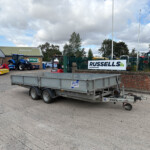Blue tractor and red equipment parked near a brick building; Russells sign visible in a gated lot.